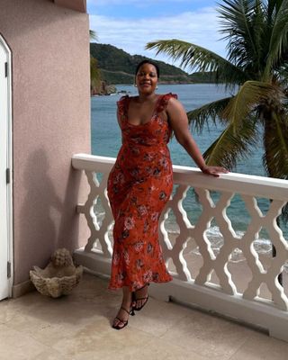 Fashion influencer Karina of Style Idealist poses on the balcony of her hotel in Antigua wearing a ruffled red floral-print dress from Réalisation and black strappy heeled sandals.