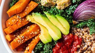 Bowl of plant-based foods including sweet potato, avocado, onion and kale