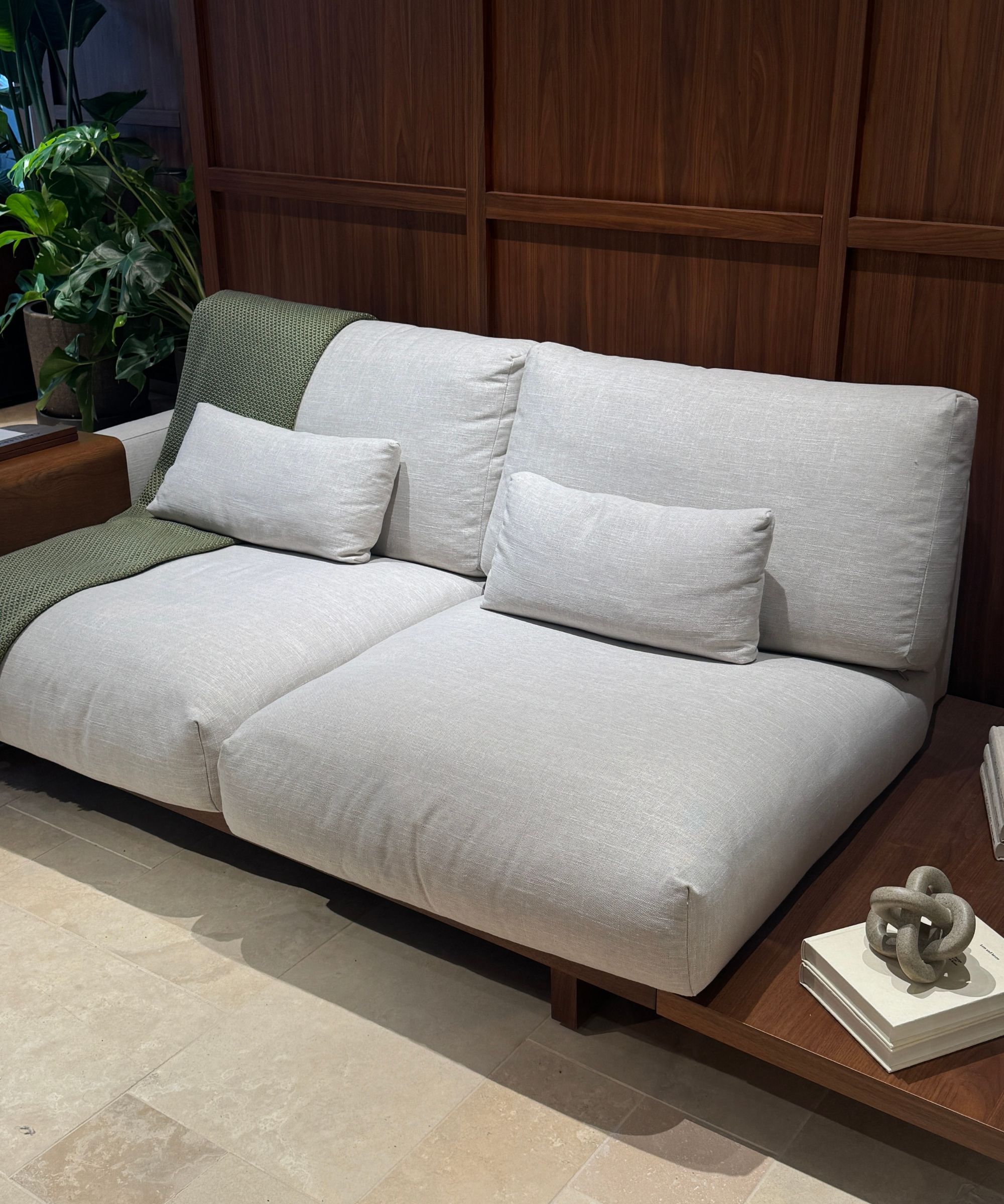 gray sofa on timber platform in front of timber panelling with travertine floors, potted plant, and side table with books and decor