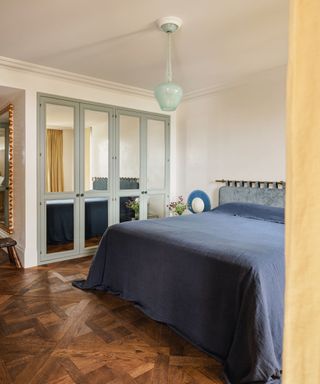 Bedroom with blue bedding and wooden flooring and light blue glass pendant light