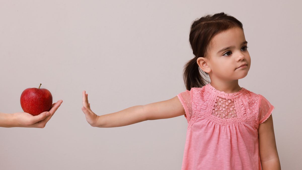 A young child with her hand out rejecting the offer of an apple