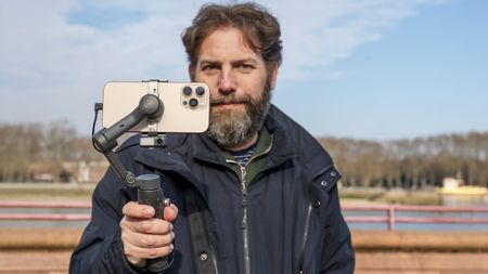 Osmo Mobile 7P in Adam Juniper's hand by river Thames with blue sky behind and iPhone 16 Pro Max in grip