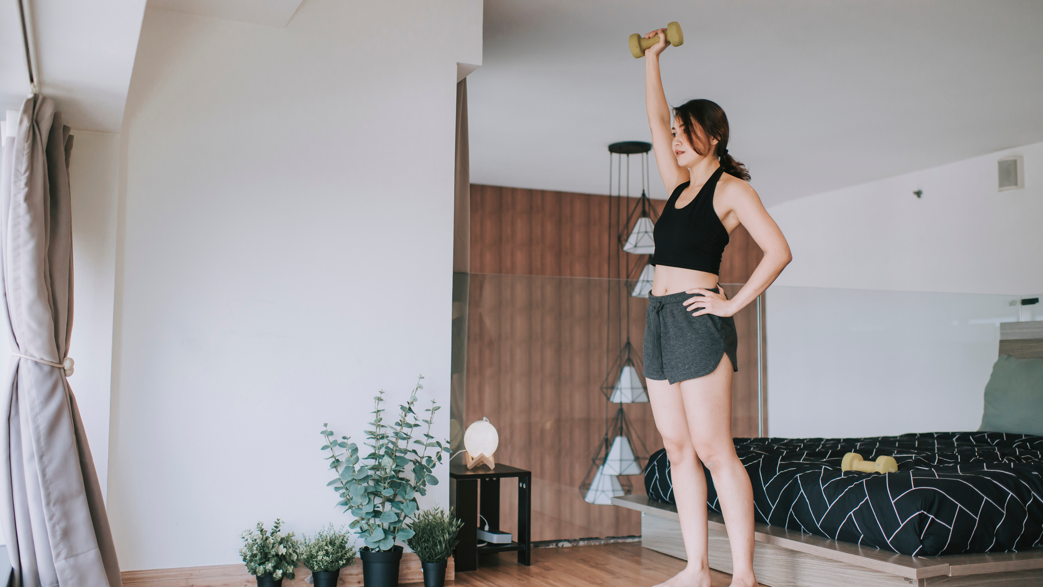 Woman exercises with a dumbbell in a bedroom