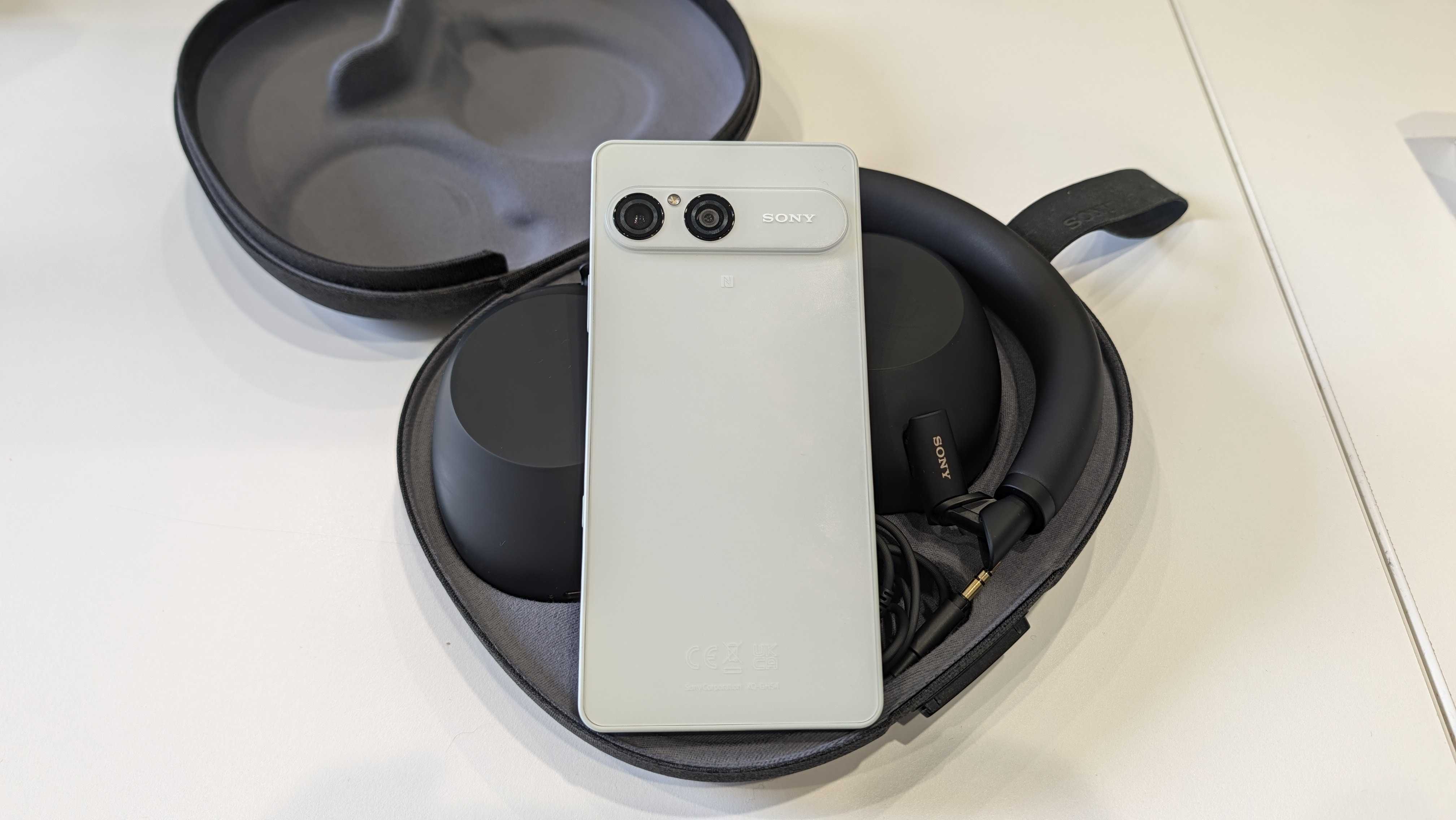 A white Sony smartphone resting on a pair of XM6 headphones in their case