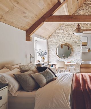 Bedroom with wooden floor, rattan rug, double bed below vaulted ceiling.