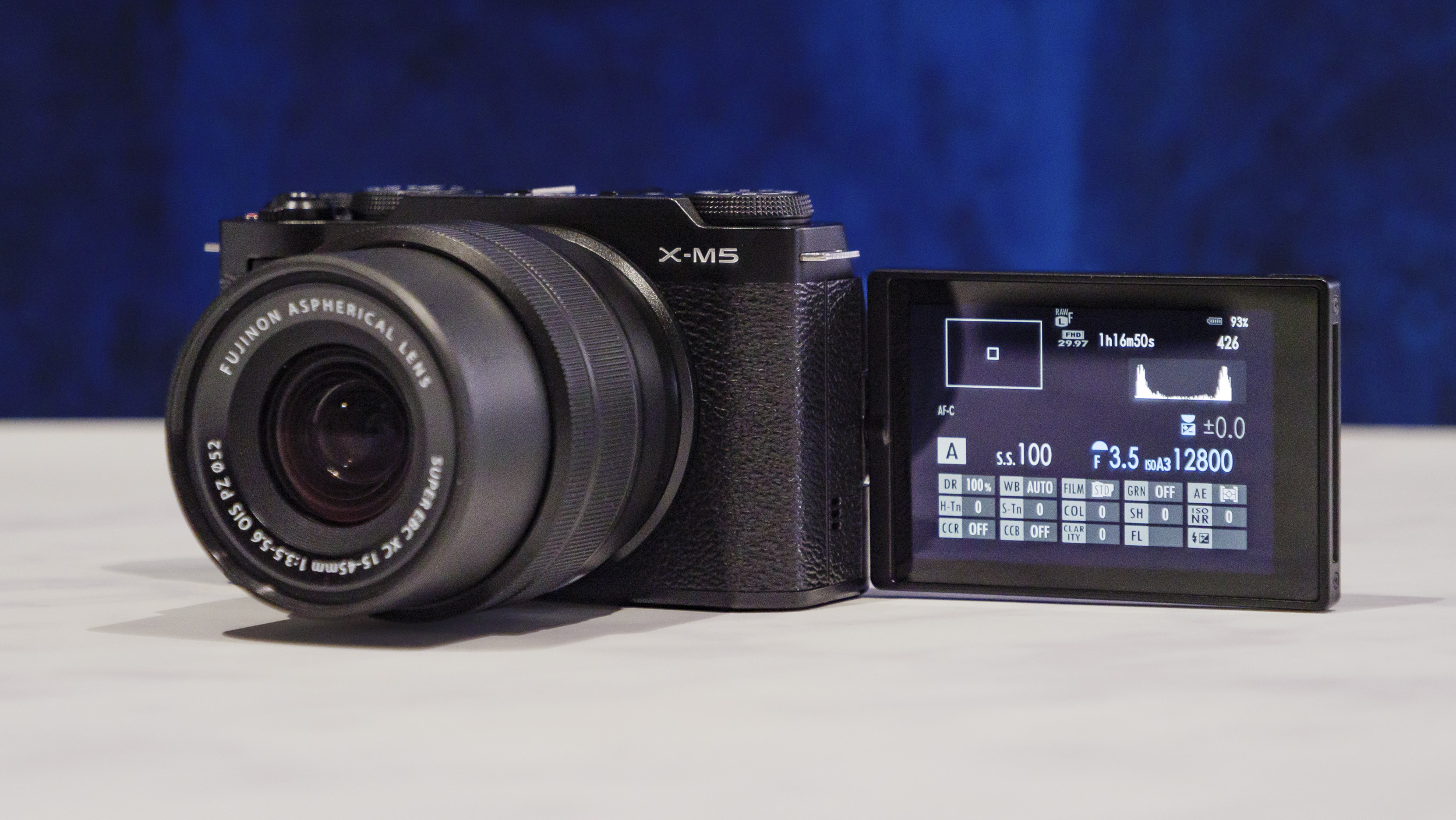 Fujifilm X-M5 camera  with flip-screen out, on a marble surface with rich blue background