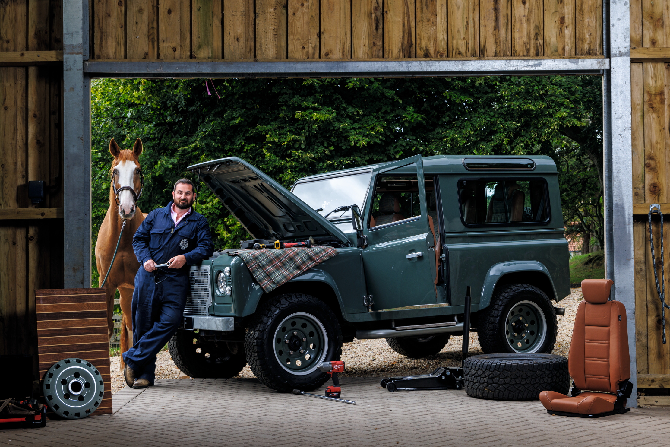 Graham Mann next to one of his cars. He is wearing a blue boiler suit. There is also a horse, for reasons that are unclear.