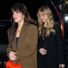 Dakota Johnson walks in front for Jennifer Lawrence wearing wide-leg trousers with loafers. Lawrence walks behind wearing wide-leg trousers with full-coverage ballet flats.