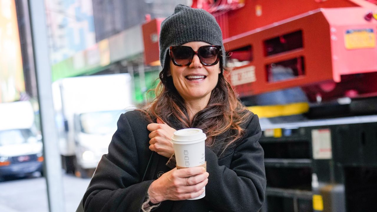 Katie Holmes wearing a black coat and a black tote bag while carrying a starbucks coffee