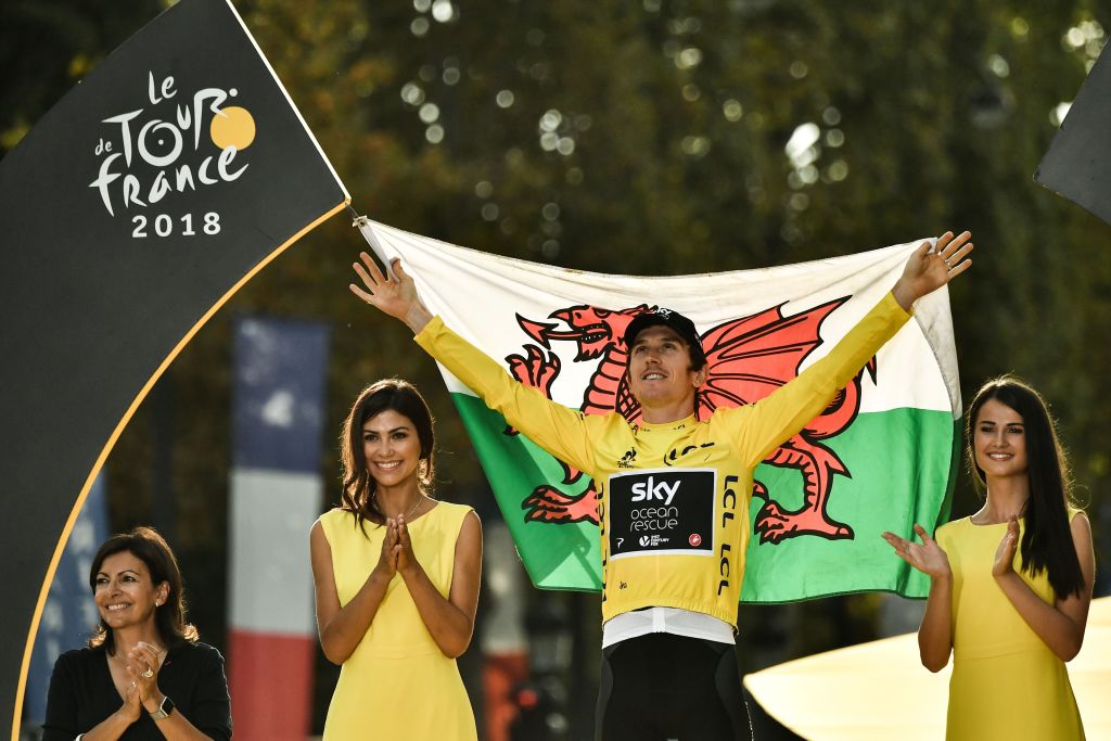 TOPSHOT - Tour de France 2018 winner Great Britain&amp;amp;apos;s Geraint Thomas holds the Welsh flag as he celebrates his overall leader yellow jersey on the podium after the 21st and last stage of the 105th edition of the Tour de France cycling race between Houilles and Paris Champs-Elysees, on July 29, 2018. (Photo by Marco BERTORELLO / AFP) (Photo credit should read MARCO BERTORELLO/AFP via Getty Images)