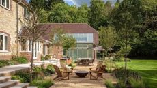 outdoor entertaining area with Adirondack chairs around a firepit on a gravel area, next to lawn, with steps up to the house