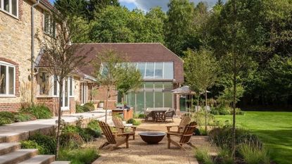 outdoor entertaining area with Adirondack chairs around a firepit on a gravel area, next to lawn, with steps up to the house