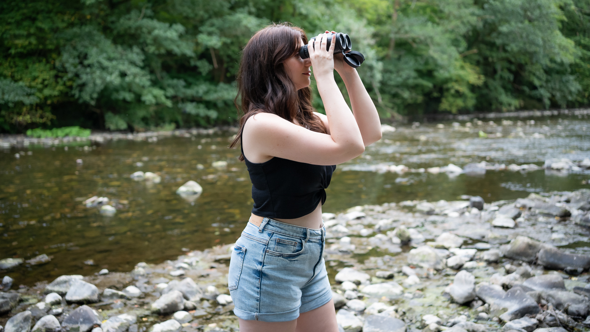 woman using the Celestron Nature DX 10x42 next to a river