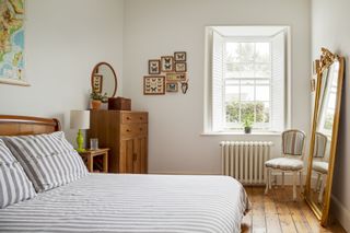 renovated bedroom with grey and white striped bedding, brown wooden furniture and window