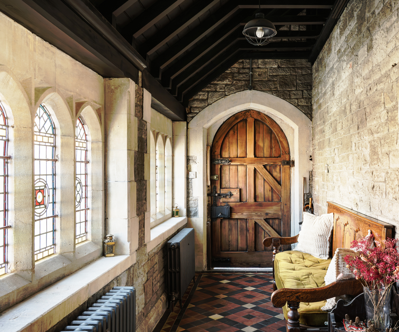 Hallway with stained glass windows to the left, bench to right and arched wooden door