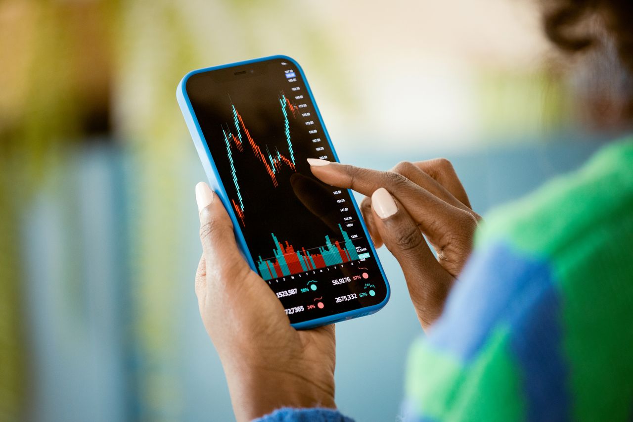 woman using smart phone at home, watching share price chart perhaps of an investment trust