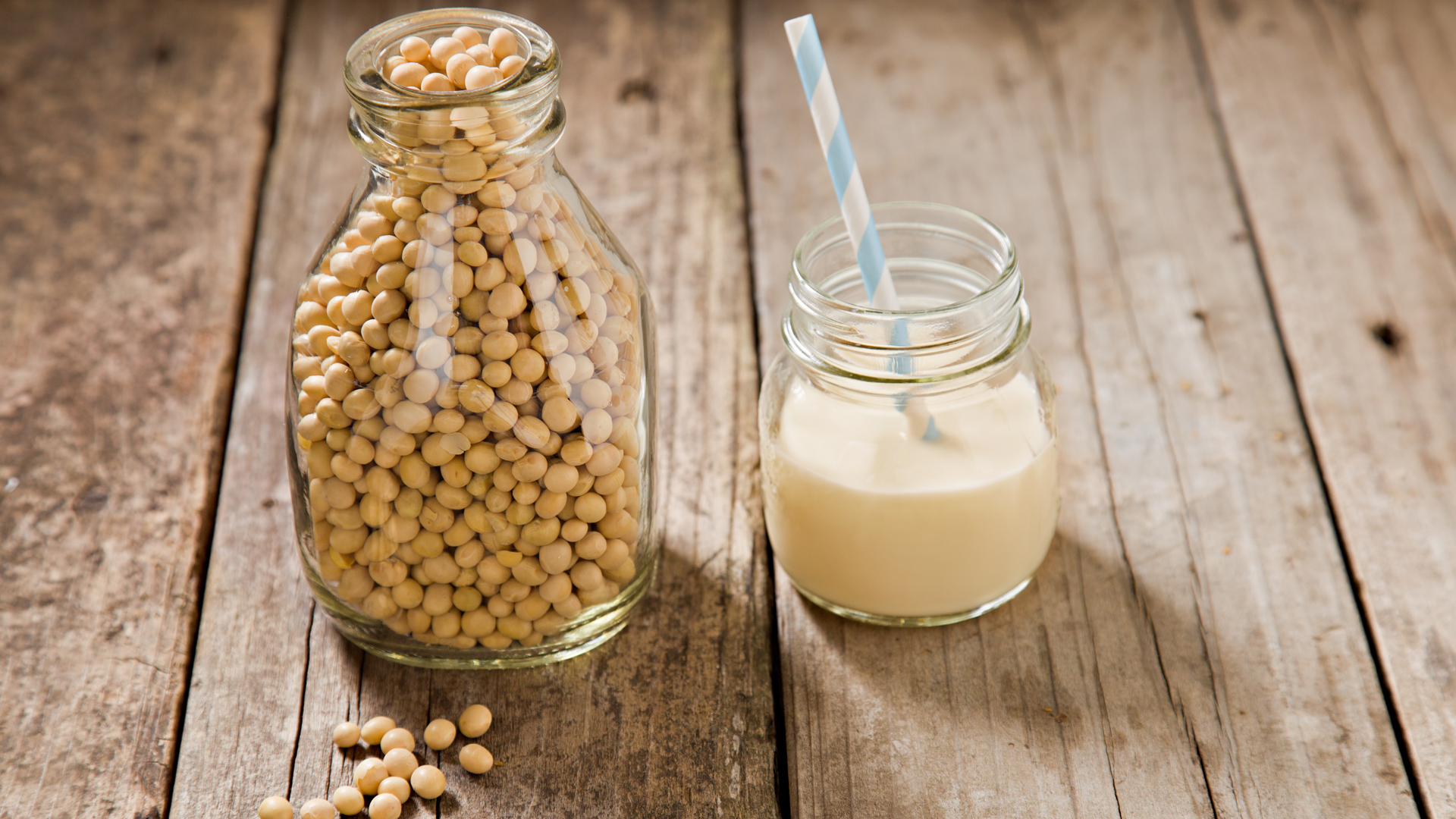 image shows a glass of soy milk next to some soybeans