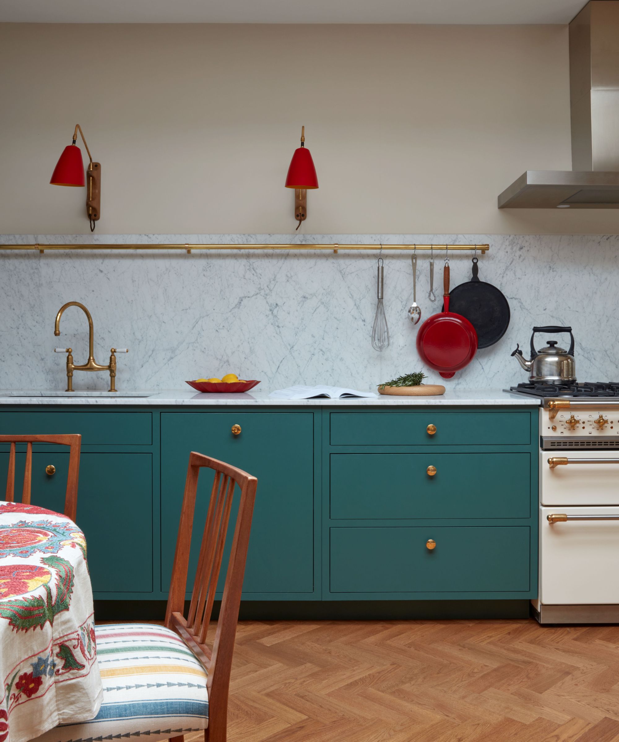 A kitchen with teal blue lower cabinets and a white marble backsplash, a gold pot rail and red wall sconces