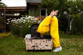 woman in yellow jumpsuit puts head down camping toilet