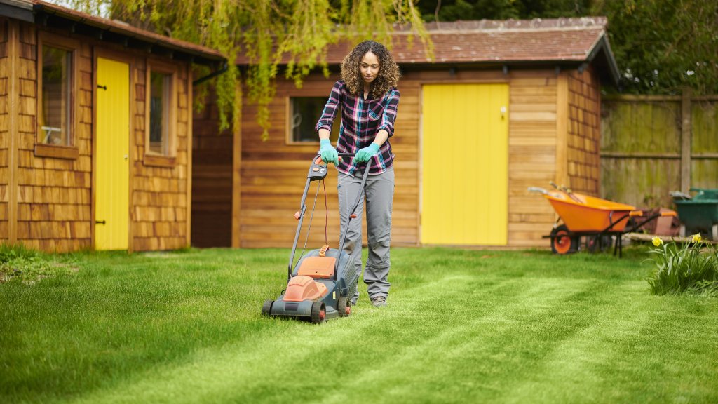 A woman mows the grass with an electric lawn mower