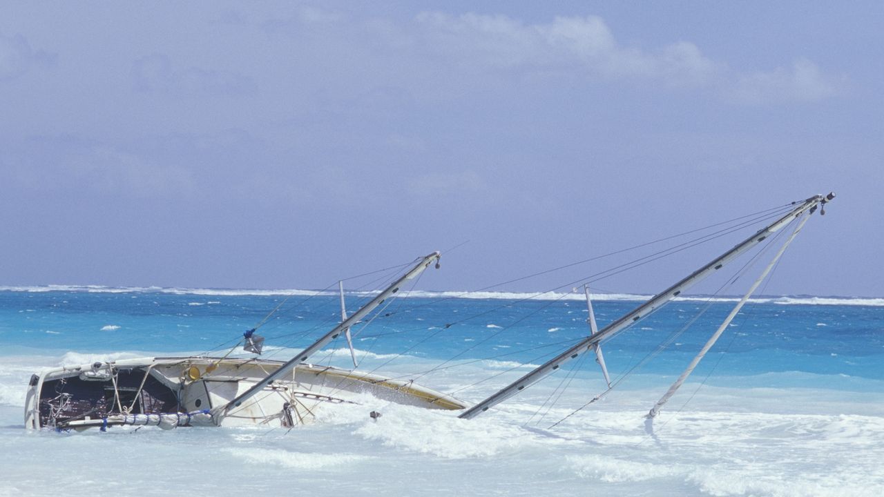 A sailboat sinks in very blue water near the beach.