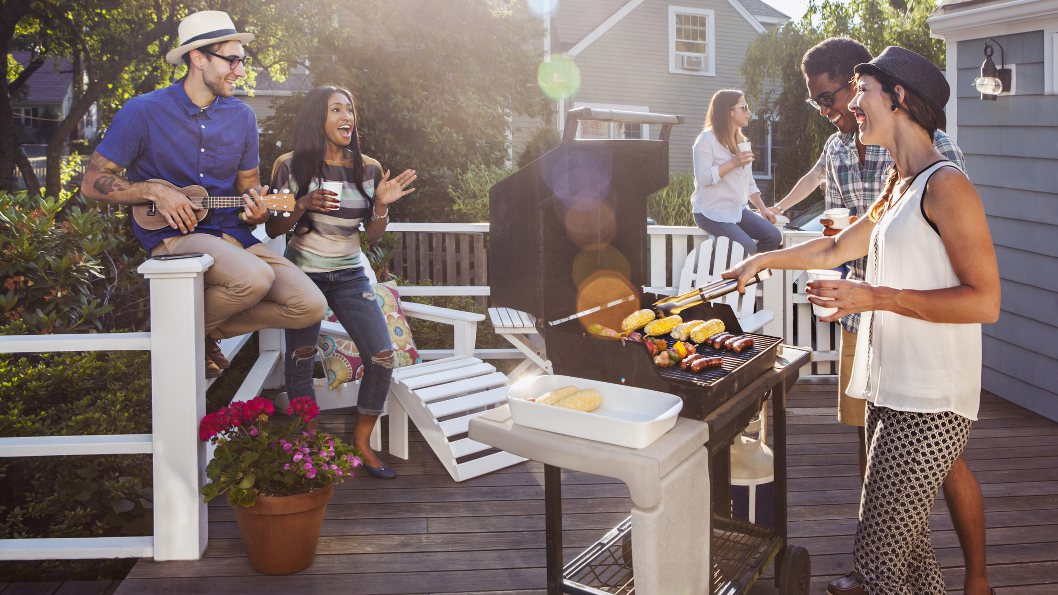 How to clean a barbecue grill: A group of friends gather around a bbq grill being used to cook sausages and corn