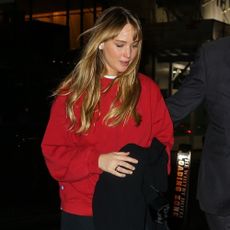 Jennifer Lawrence walks alongside a bodyguard years black trousers that she's rolled up at the ankles with a red oversized knit and a pair of garden clogs.
