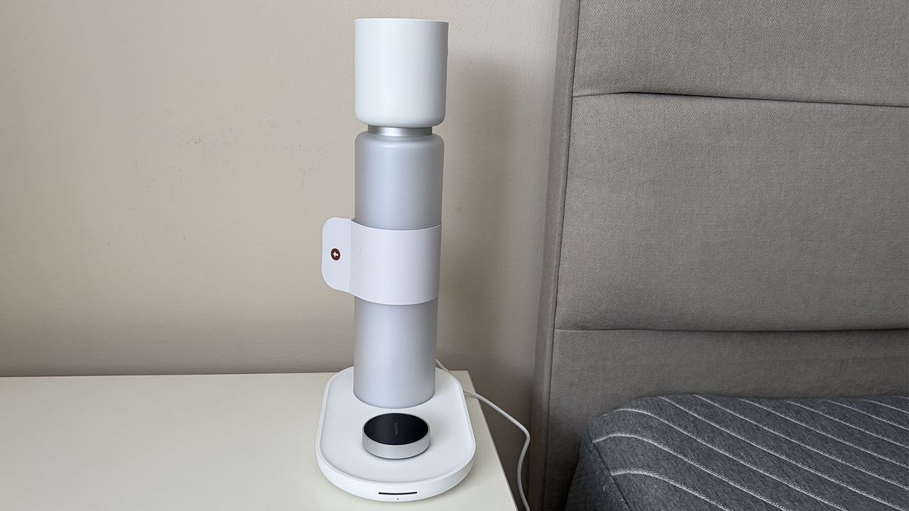 The Sleepal AI Lamp on a nightstand next to a mattress in the reviewer's bedroom, with the tag still on.