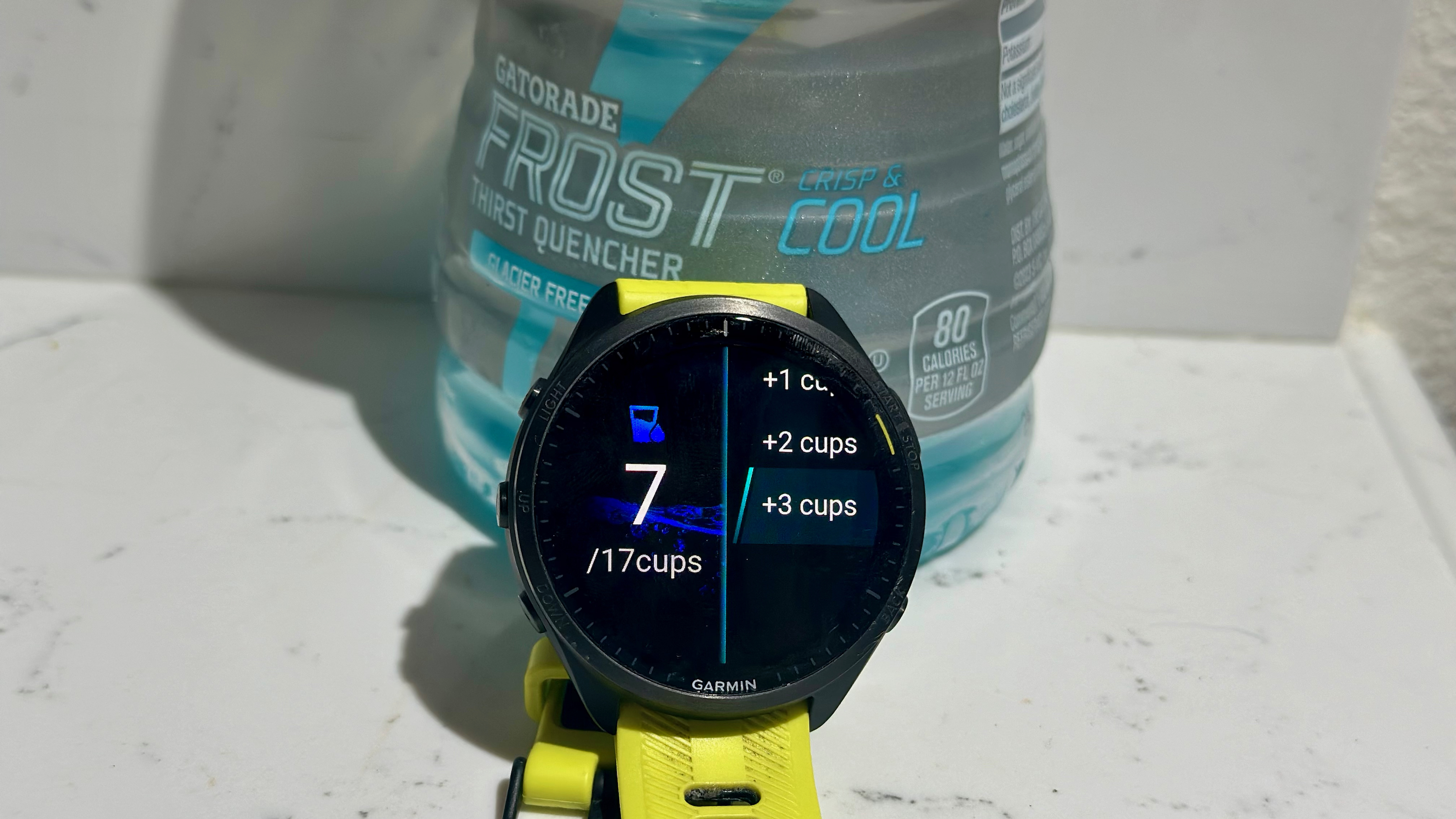 El Garmin Forerunner 965 muestra la aplicación de seguimiento de datos de hidratación, sentado frente a una botella de Gatorade.