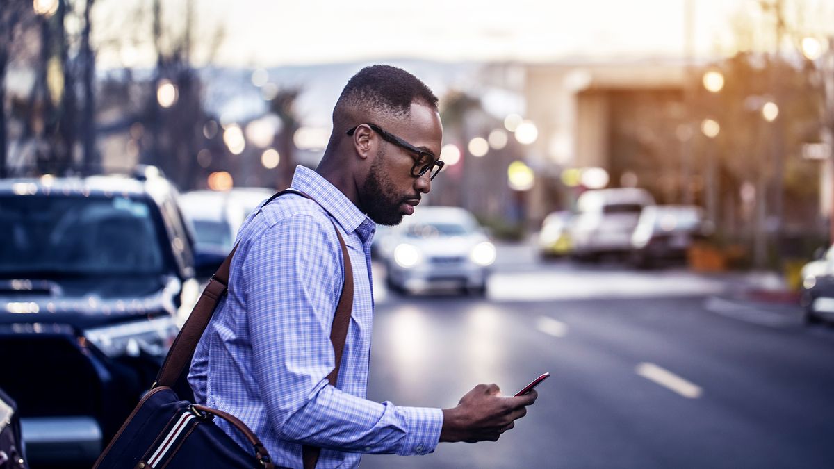 A businessman crossing the road while looking at his smartphone and wearing a shoulder satchel