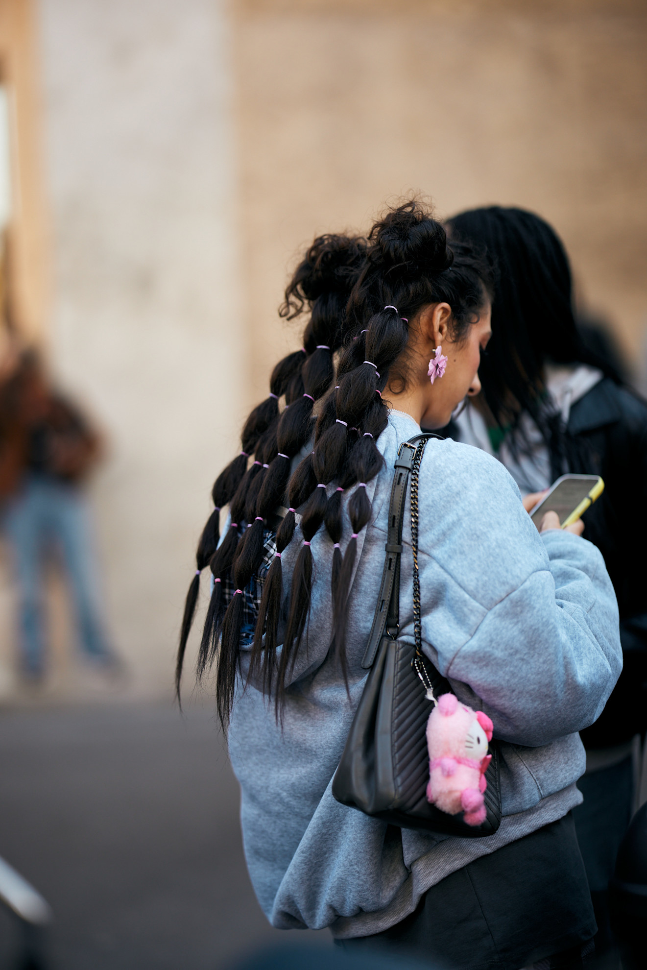 a woman with long bubble braids wearing a denim jacket and a black bag with a pink charm