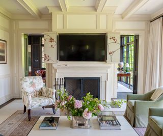 traditional living room with cream panelled walls, fireplace, green armchairs and patterned armchair, large coffee table with pink flowers in vase