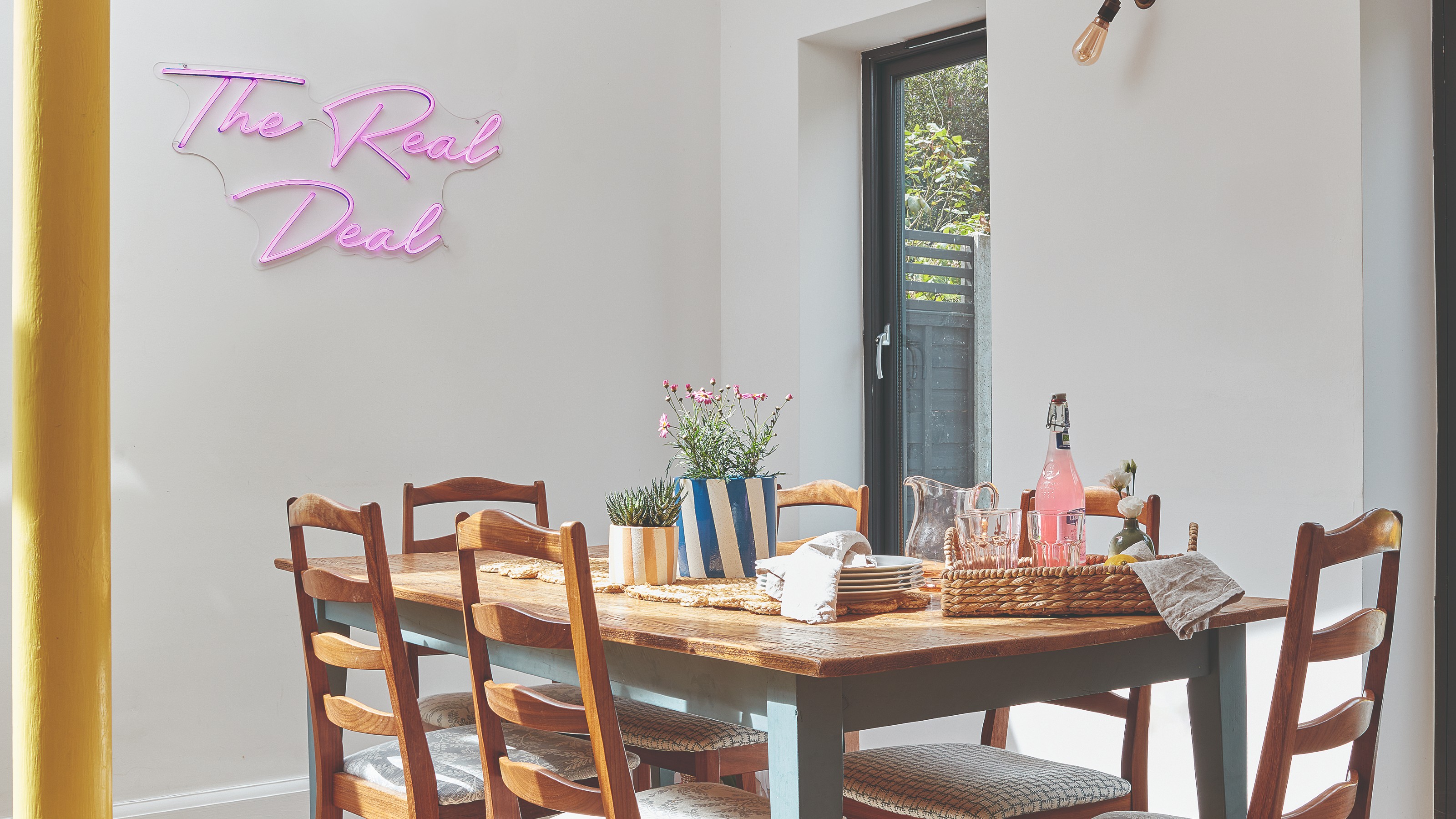 A dining area with a neon light on the wall and the table decorated with two potted plants in striped plant pots
