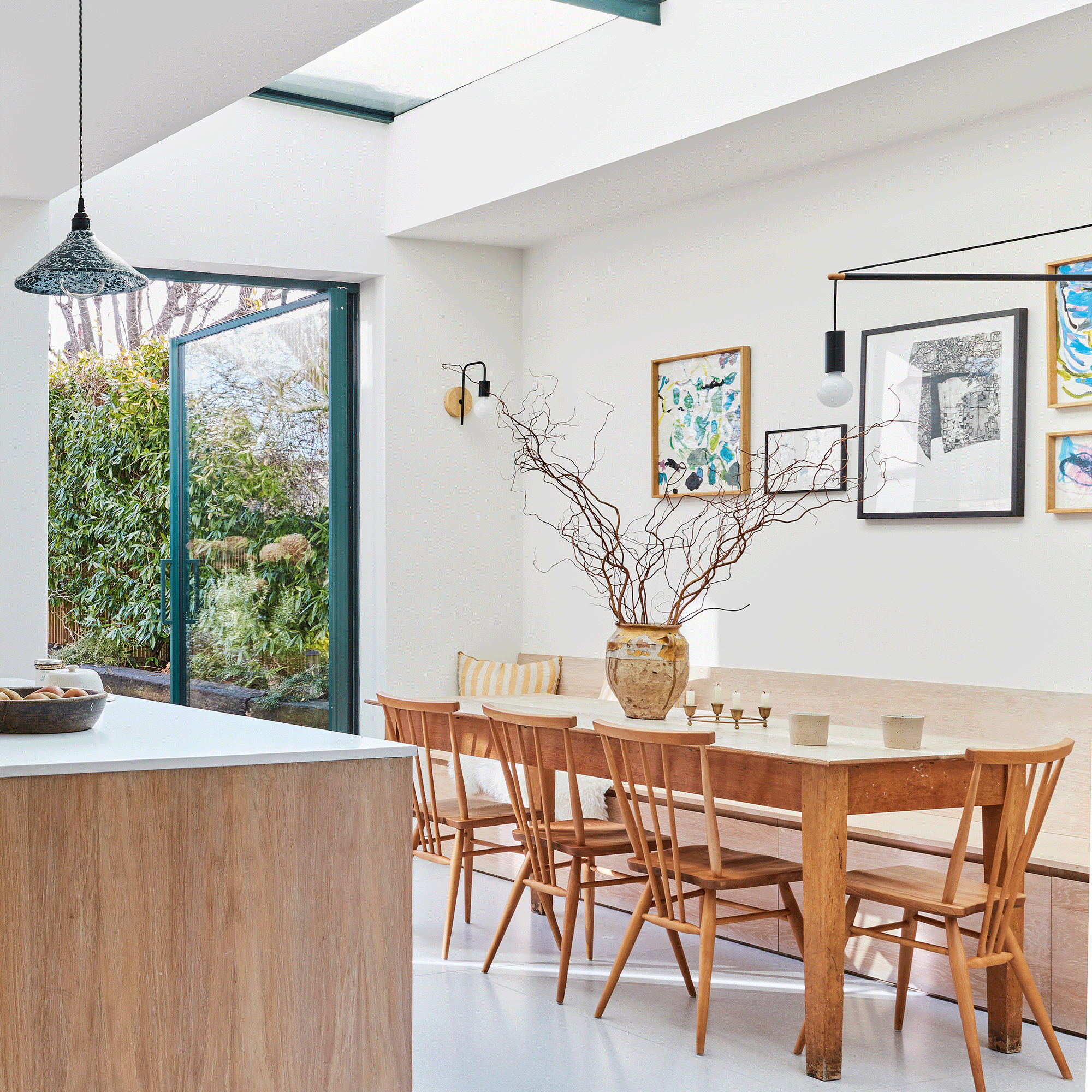 a kitchen diner with white walls and wooden dining furniture with green framed glazing in both the skylight and pivot patio door
