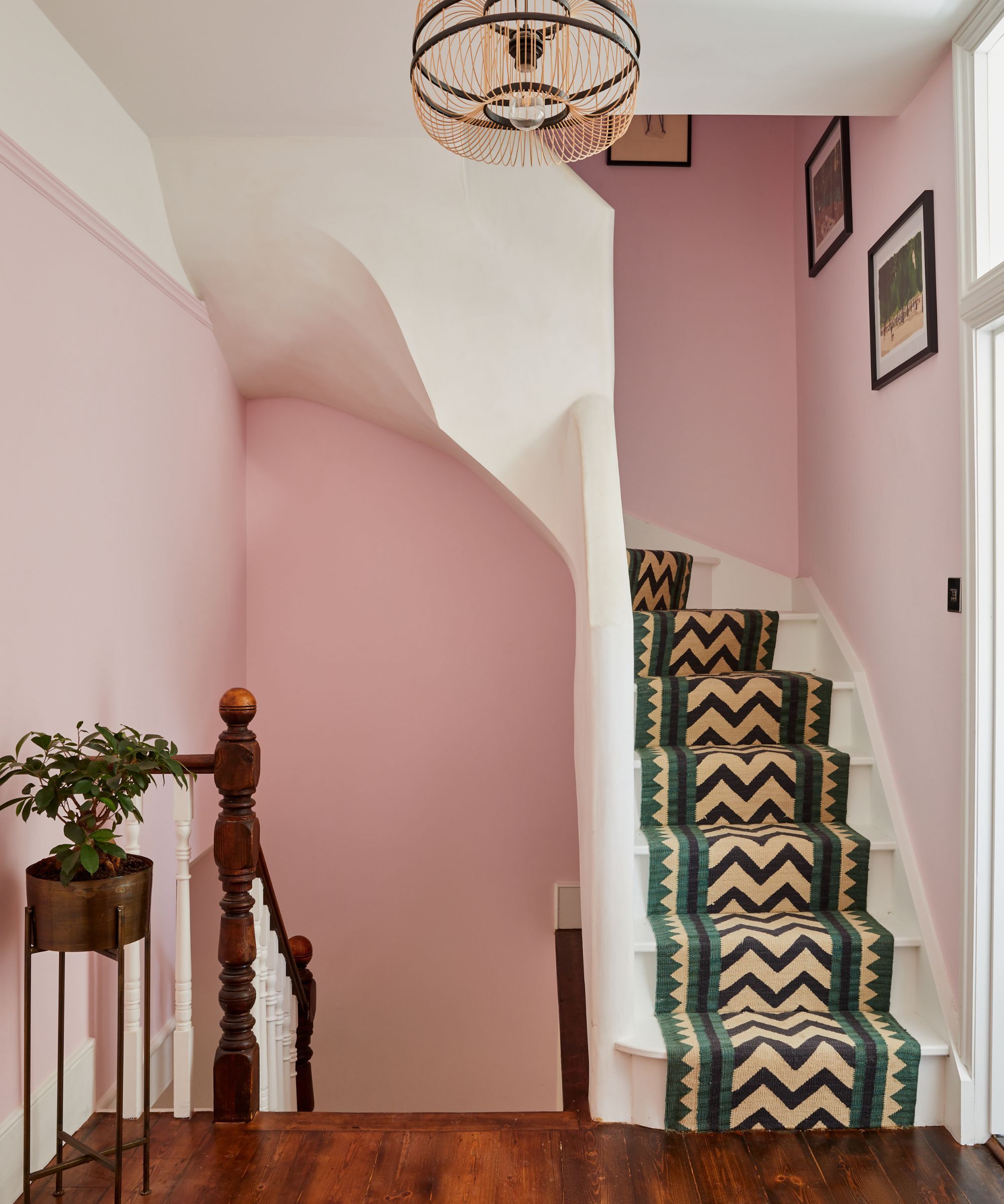 A staircase with pale pink walls and white stairs with a green, black and camel coloured Aztec print runner up the middle.