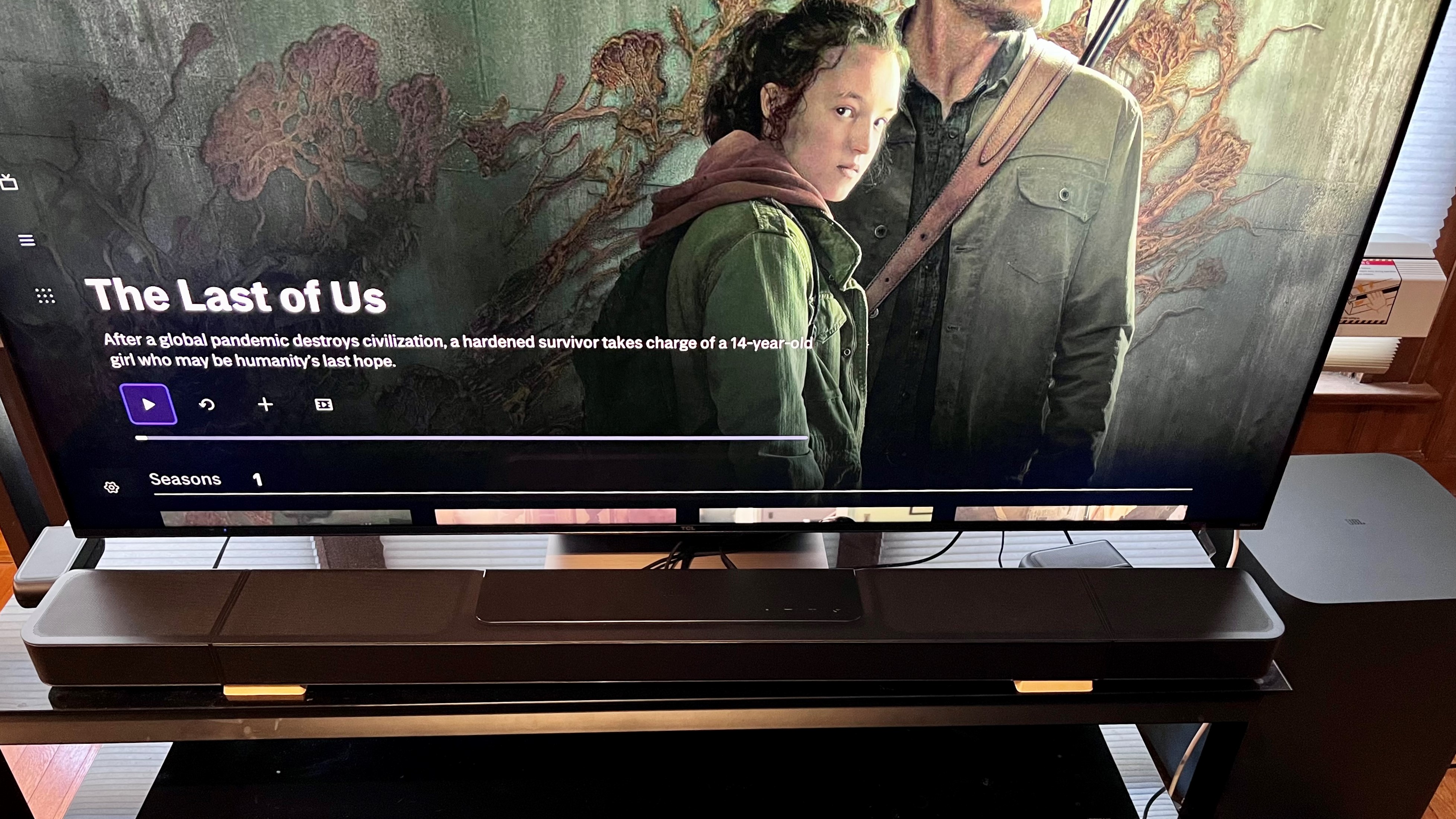 JBL 1300X soundbar on TV stand with TV showing the last of us