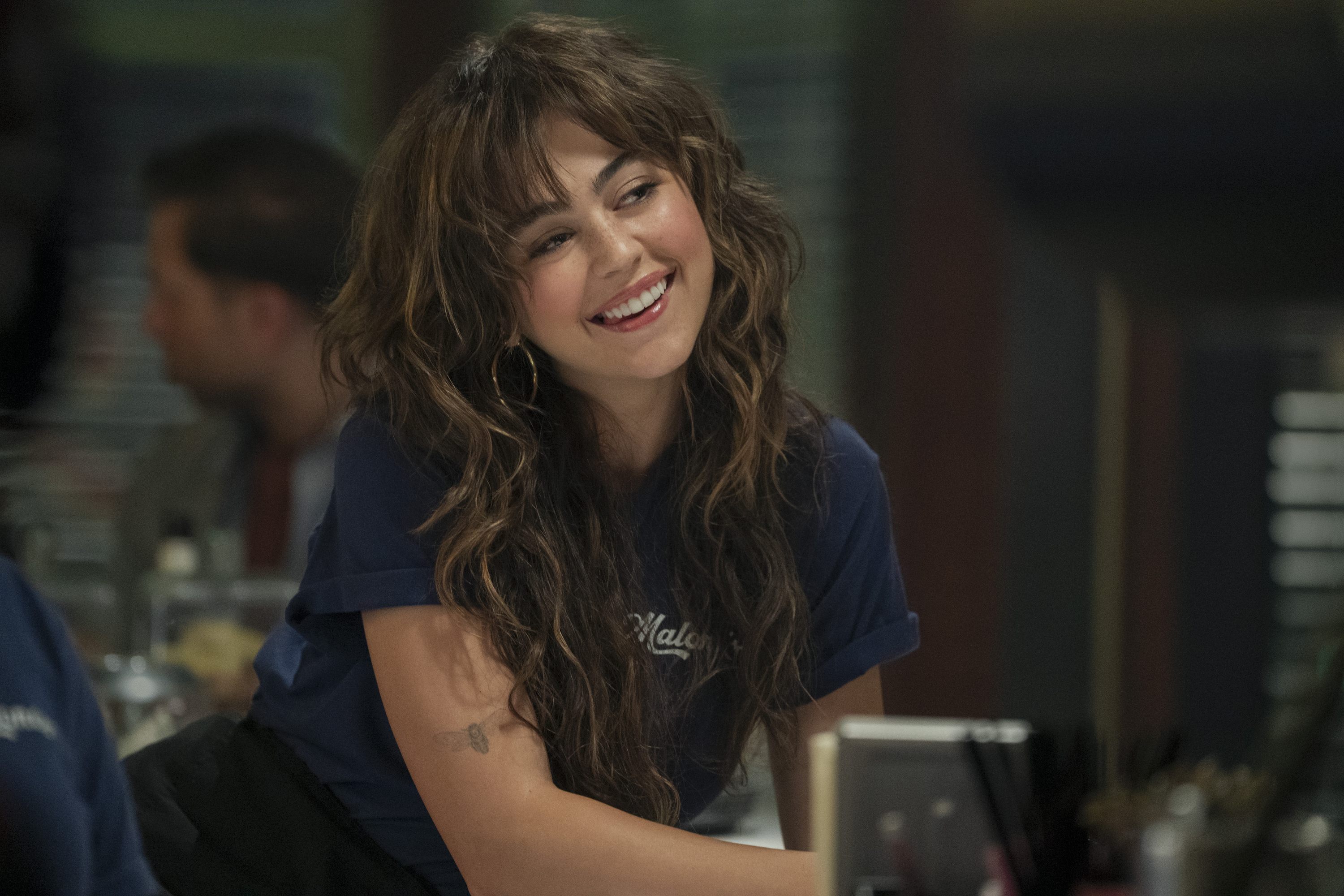 Allie (Mika Abdalla) smiles and leans over a counter while working concessions in off campus season 1