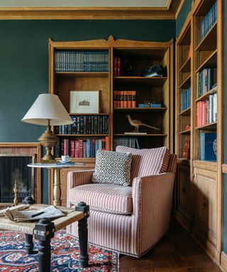 Corner of a green living room with wooden book shelves and striped armchair