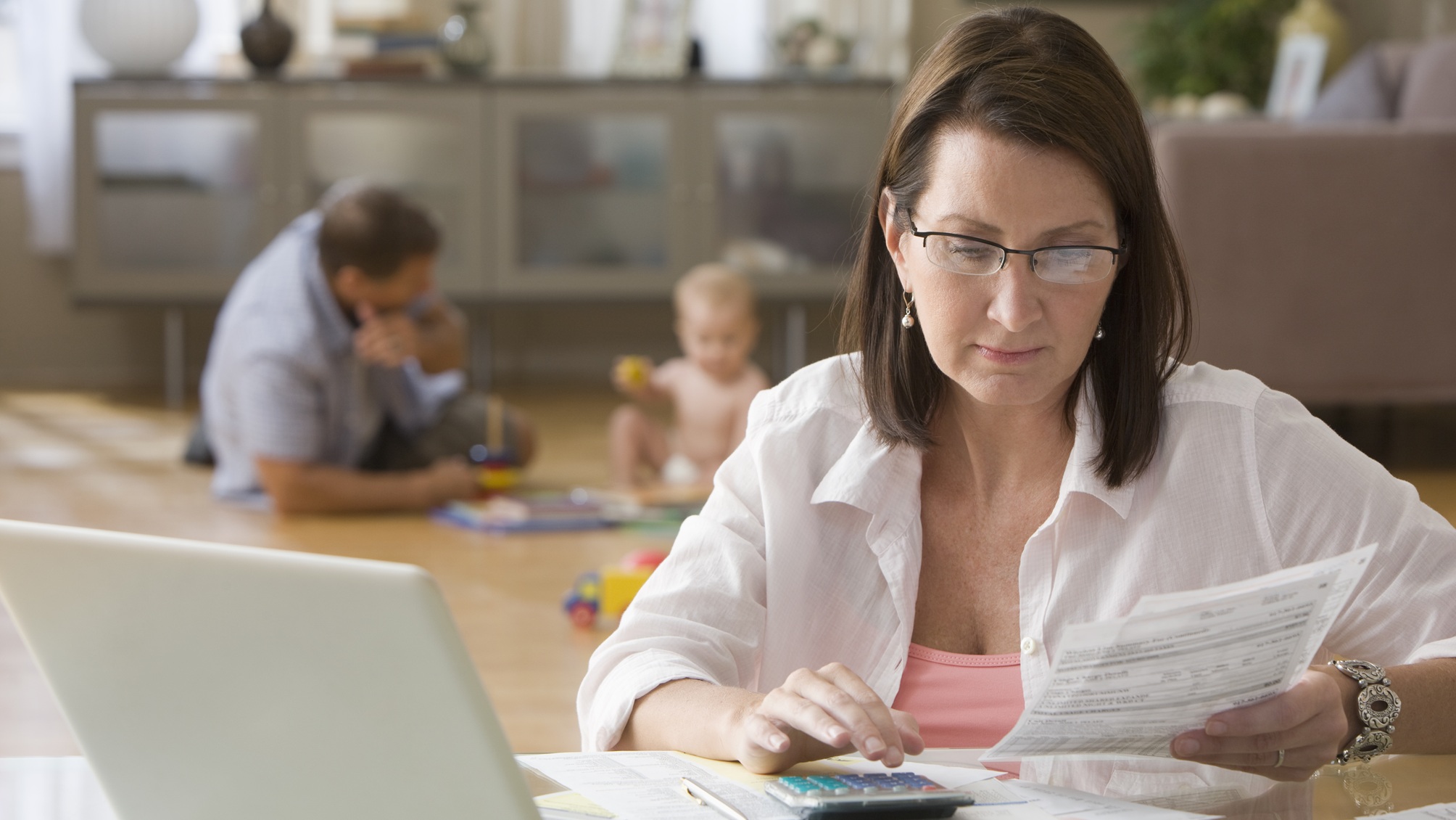 A woman uses a calculator while looking at financial documents at her dining room table.