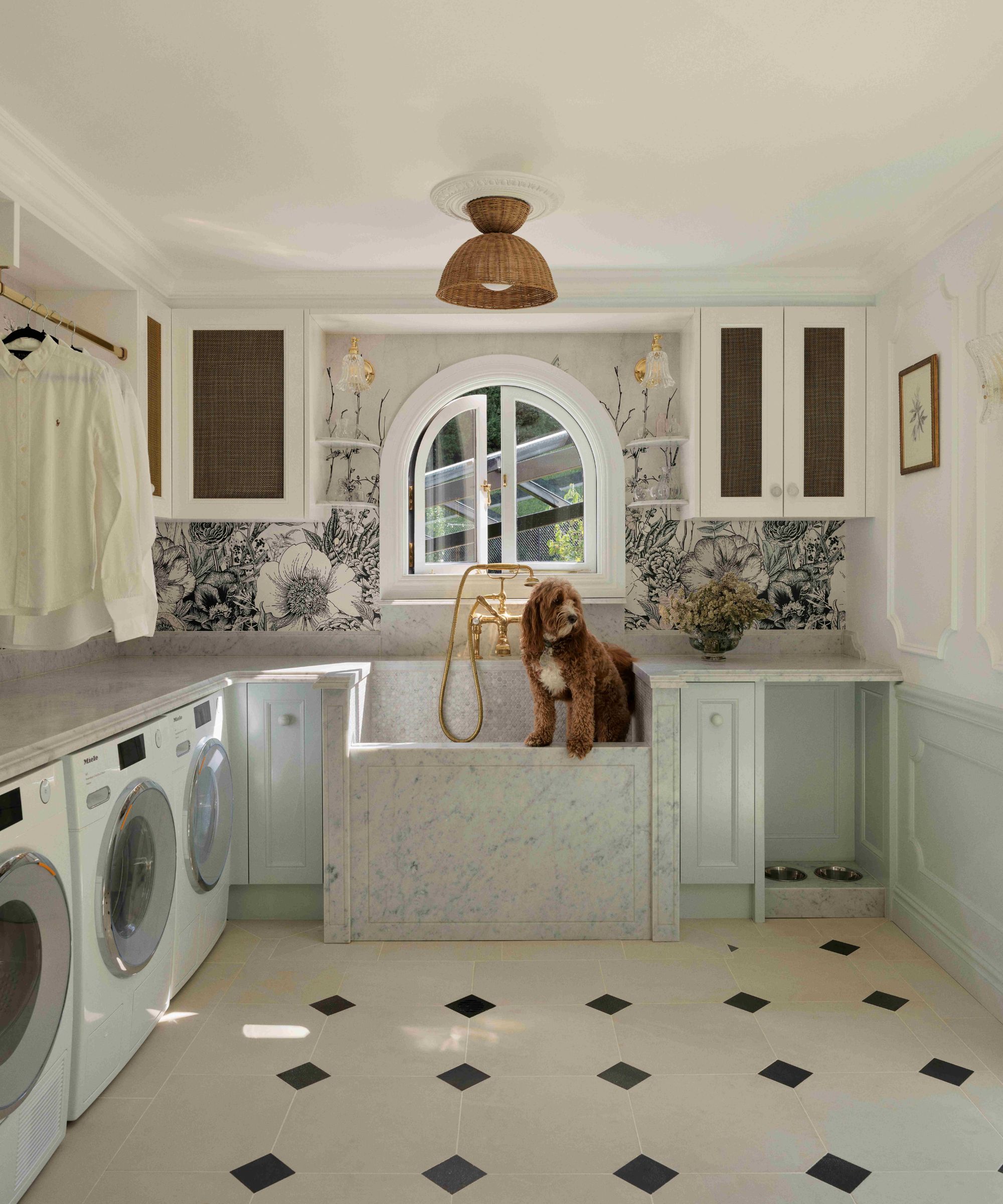 a doodle dog standing in a custom green marble dog wash station in a laundry room with botanical wallpaper and tiled floor