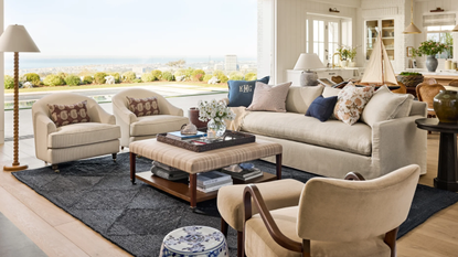 a living room with beige furniture, an upholstered coffee table, a blue jute rug, decorative pillows, and a view that looks out over a pool