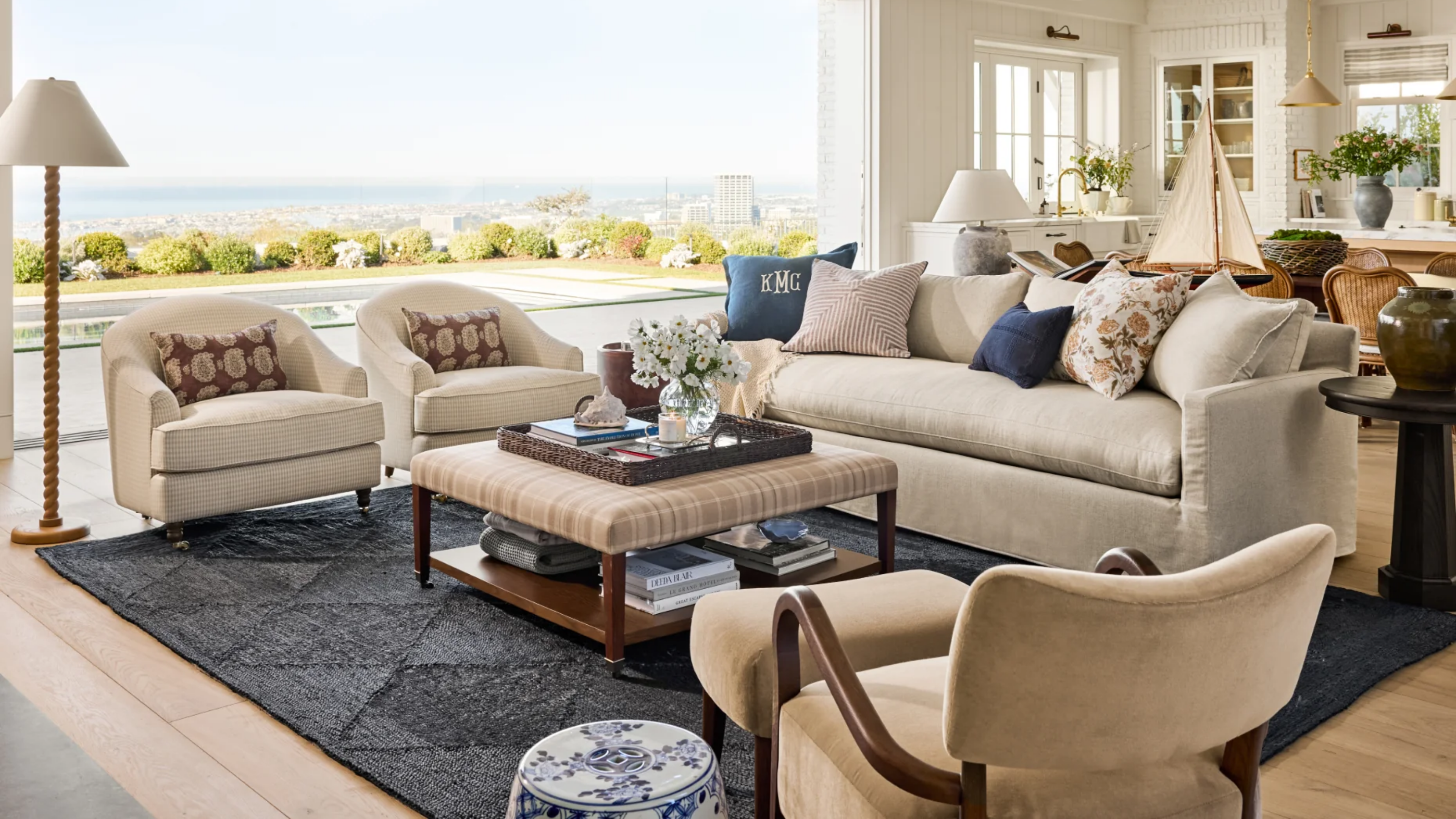 a living room with beige furniture, an upholstered coffee table, a blue jute rug, decorative pillows, and a view that looks out over a pool