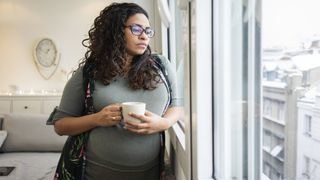 A pregnant woman looks thoughtfully out a window. 