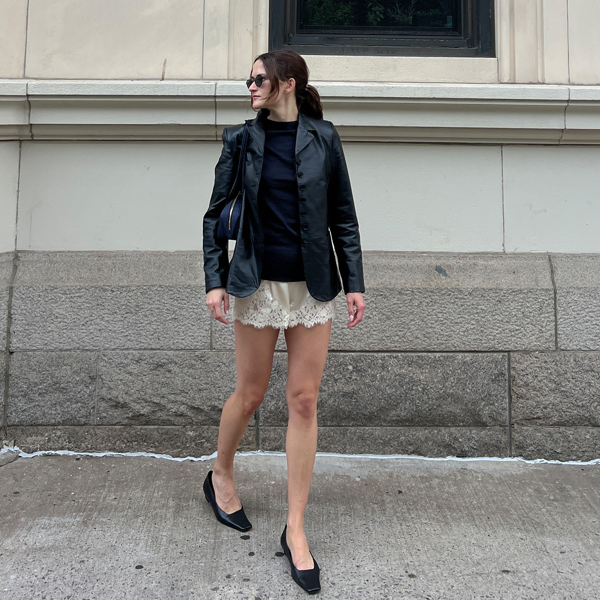 Eliza Huber wearing a leather blazer, navy sweater, ivory lace shorts, and black flats.
