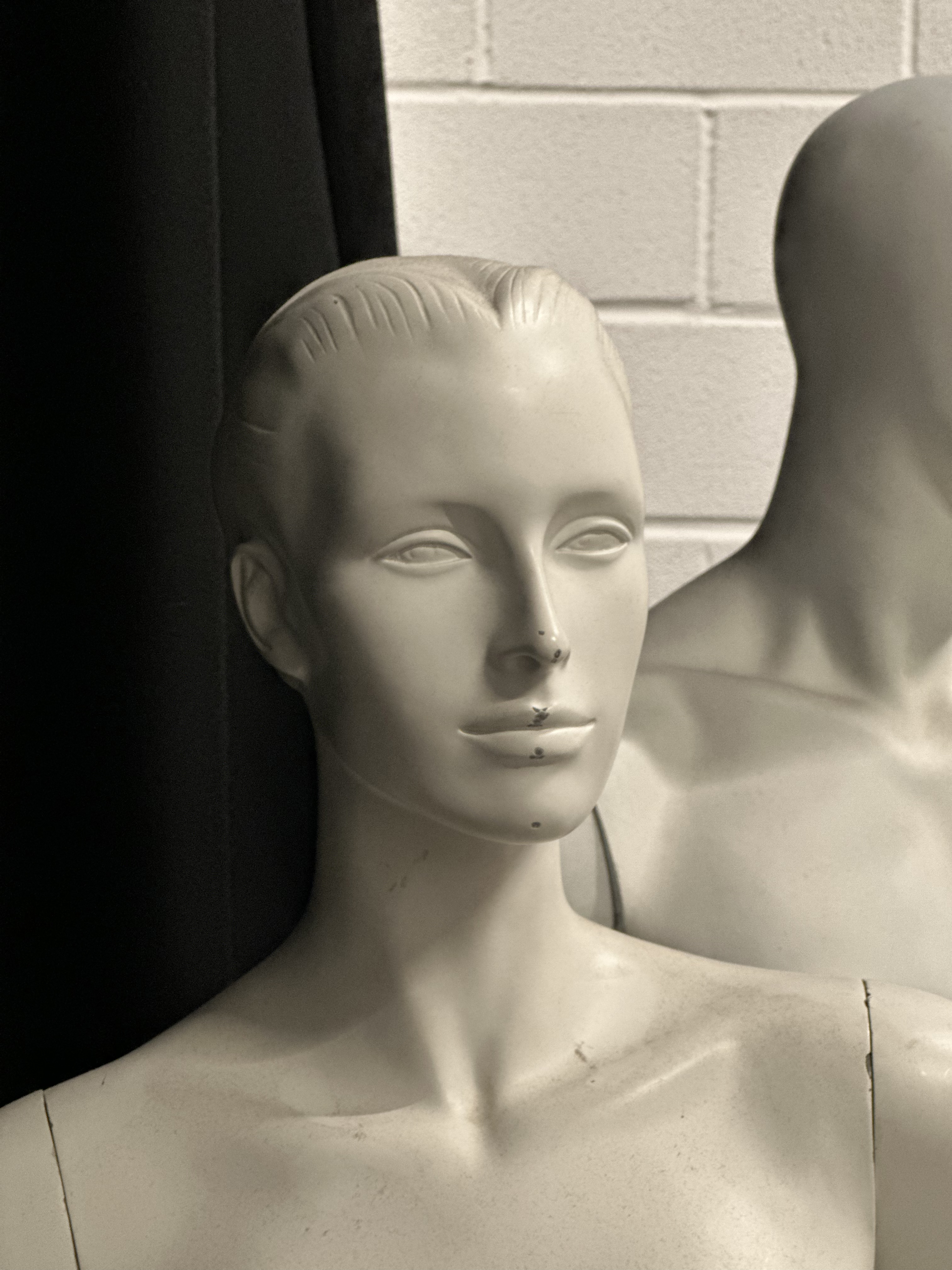 A photo of a white mannequin with a black curtain and white wall in the background.