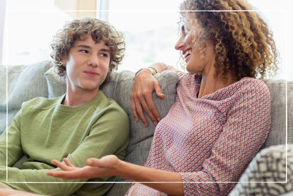 Mother and teenage son smiling together as they sit on the sofa at home