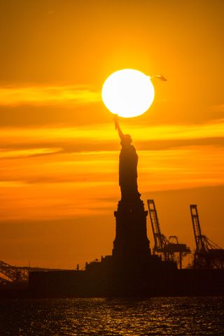 Using seven HDR images to create a composite, the photographer emphasized the sun reflecting on the water without over exposing the sun itself. Above Lady Liberty, a helicopter clears the solar disc with contrails glowing brightly behind it.