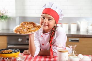 Girl in apron holding up waffles on a plate she's made at home