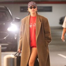 Hailey Bieber in red micro shorts, a red sweatshirt, and tan maxi coat