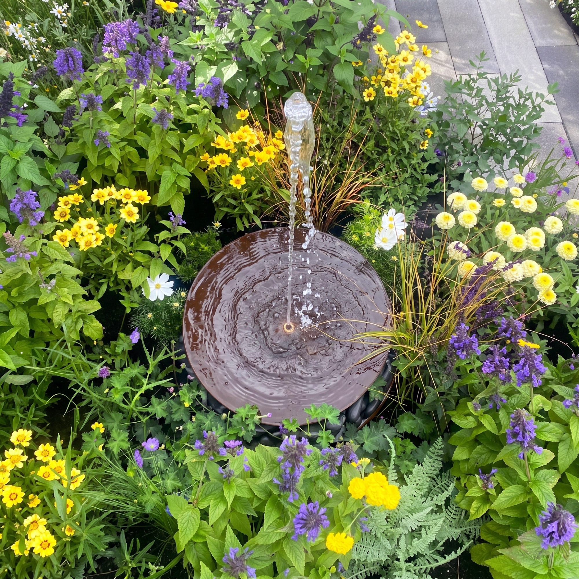 garden water feature surrounded by yellow and purple flowers